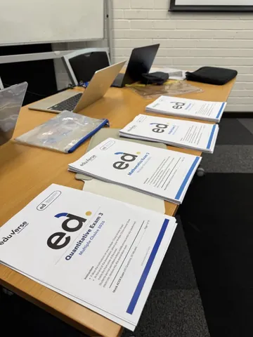 Exam papers with the EduVerse mark laid out on a desk beside two laptops