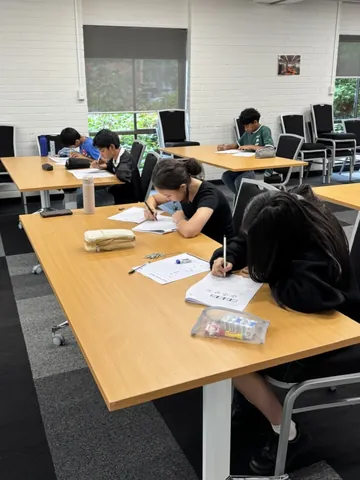 Students writing at a long table in a bright room